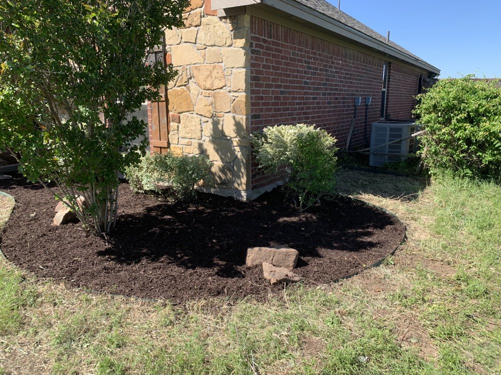 Fresh mulch bed installed around brick chimney corner with manicured trim